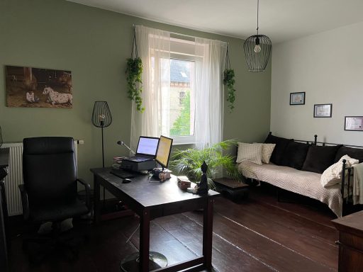 Ein gemütliches Arbeitszimmer mit Schreibtisch, Stuhl und einer Couch in sanften Grüntönen.