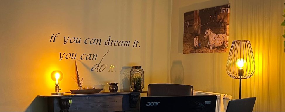 Gemütliches Arbeitszimmer mit einer Lampe, einem Schreibtisch und inspirierender Wandschrift.